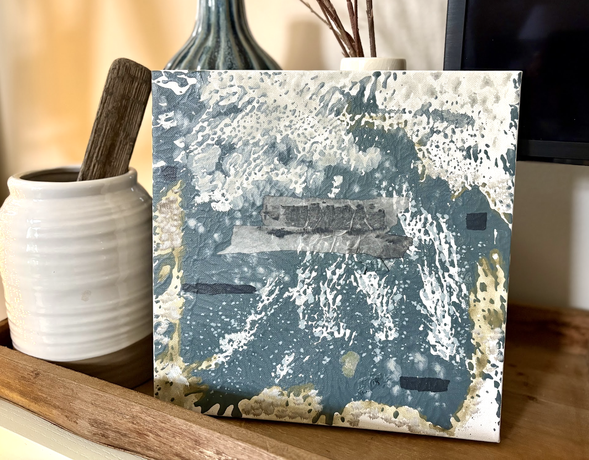Abstract art in a tray with blues, greens, neutrals and texture next to rustic vase and tray in a warm living room