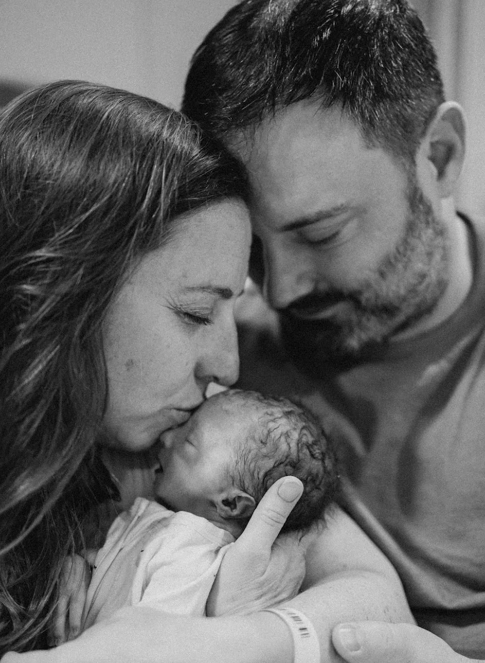 A woman and a man holding a newborn baby, touching foreheads and noses together in a tender moment, all with closed eyes.