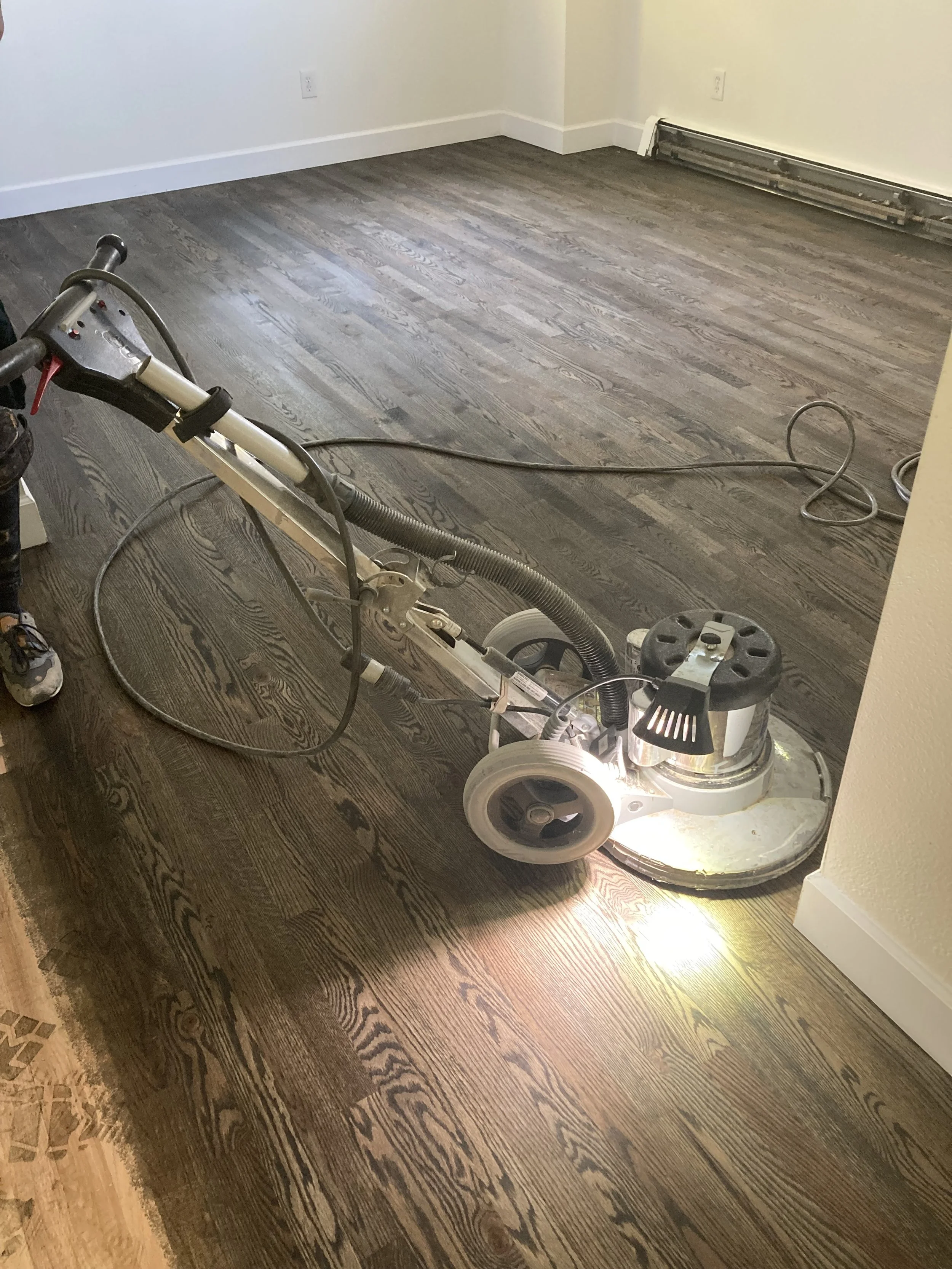 A room with newly sanded hardwood floors and a floor sander machine.