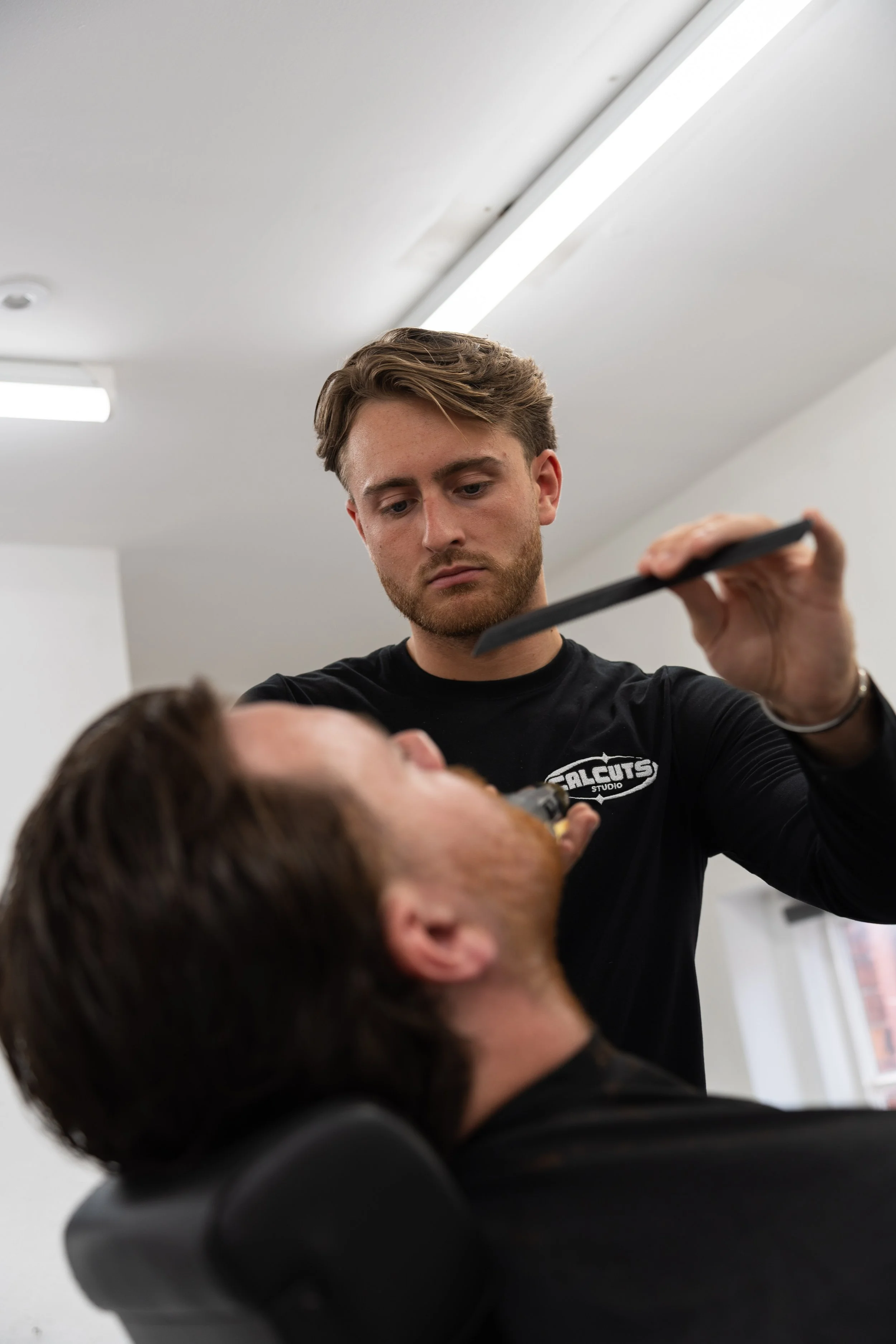 A barber trimming a man's beard at a barbershop.