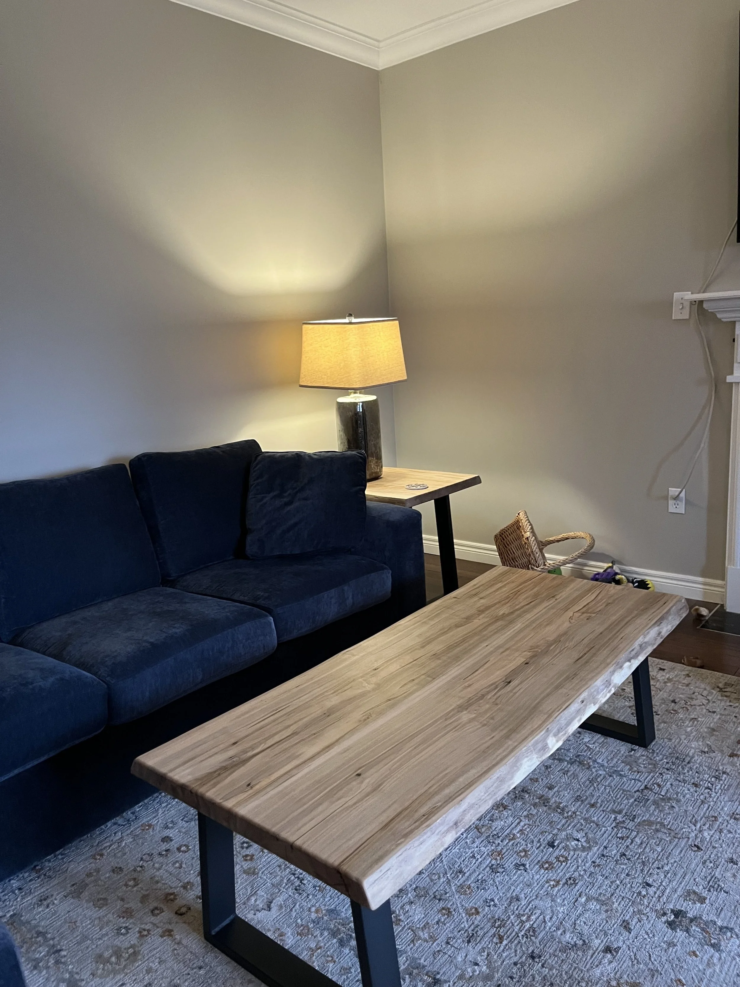 A living room with a beige wall, a blue couch, a wooden coffee table, a side table with a lamp, and a woven basket on the floor.