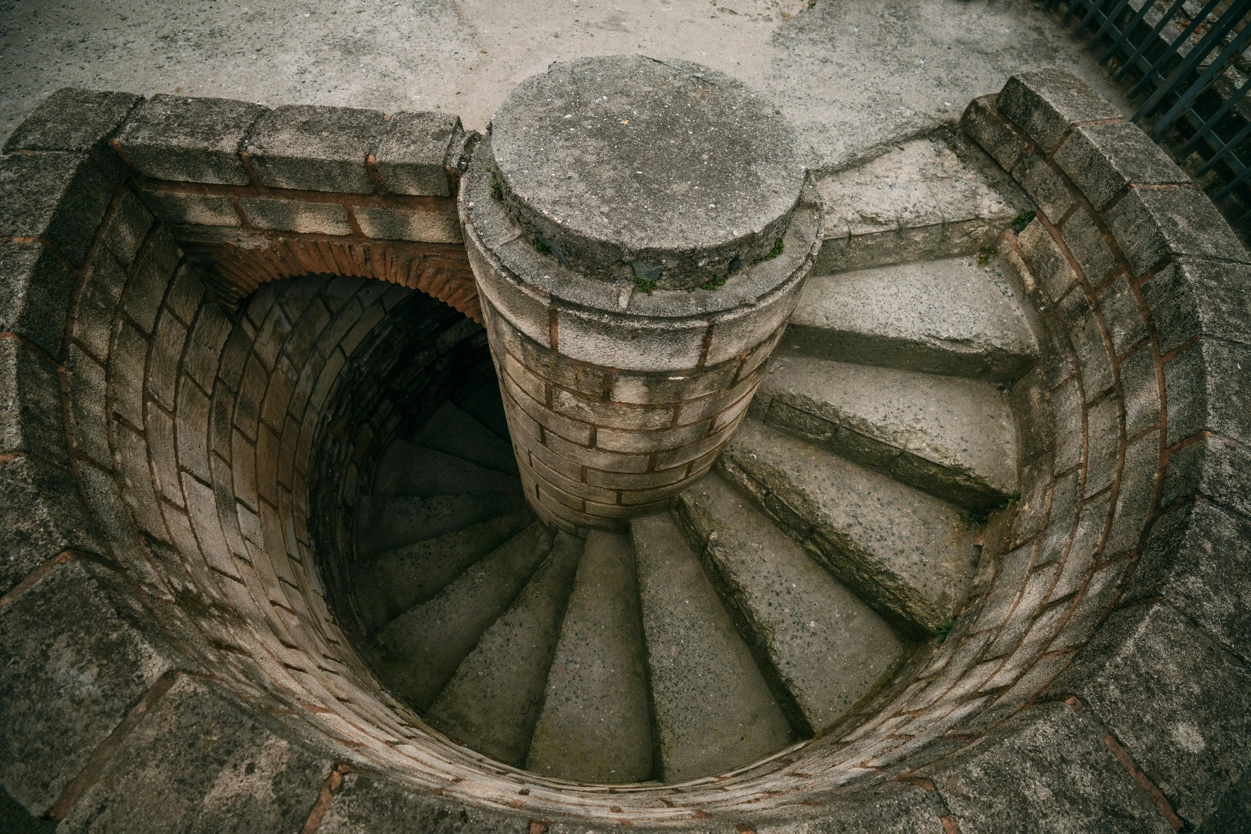 A flooded subterranean stone corridor with arched pillars and a spiral staircase descending into dark, still water.