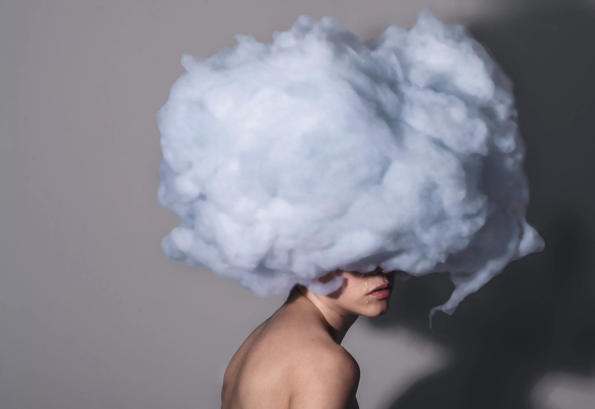 A person with bare shoulders has two large, fluffy cloud formations over their head, obscuring their face.