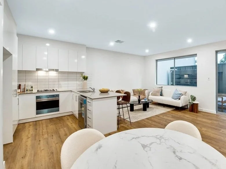Modern open-concept living room and kitchen with white cabinetry, hardwood floors, and a dining table in the foreground.