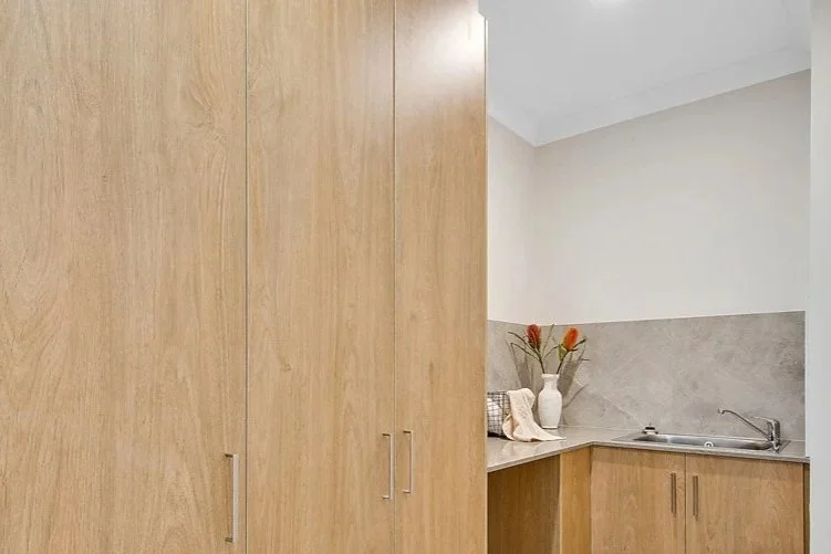 Kitchen corner with light wood cabinets, a small stainless steel sink, and decorative vases with flowers on the countertop.