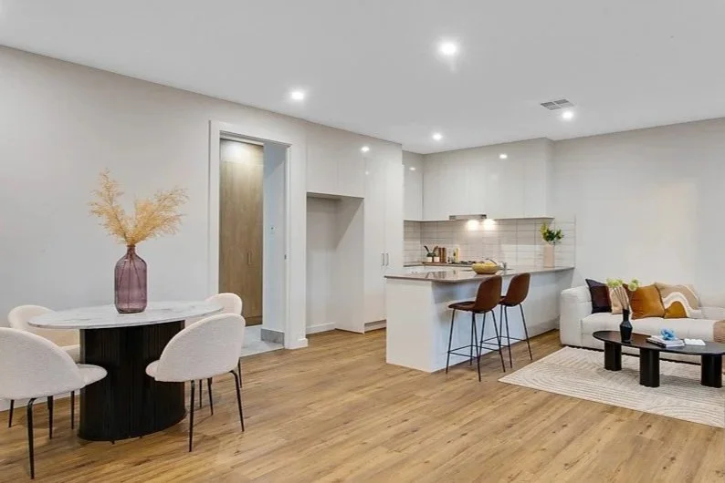 Open-concept living and dining area with a kitchen, round dining table with chairs, sofa, coffee table, and minimal decor.