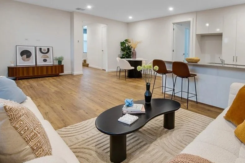 Living room with wooden floors, modern furniture, artwork on a sideboard, a black coffee table with decor, and a bar area with chairs.
