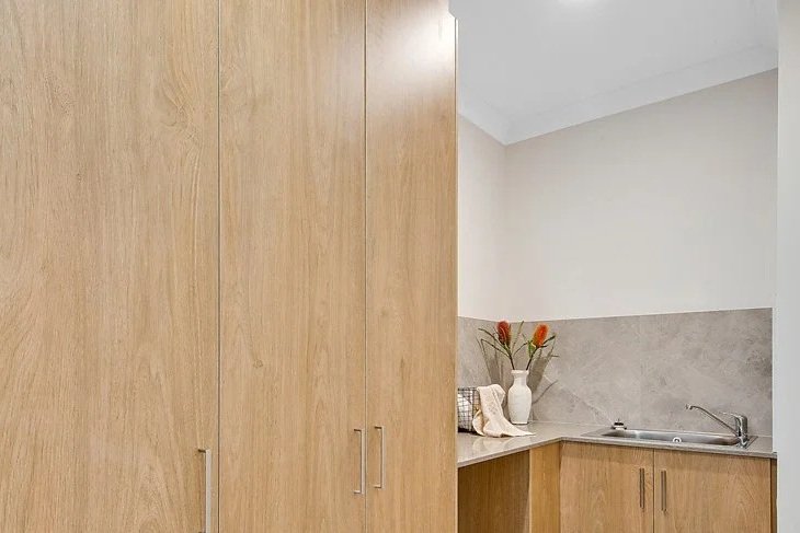 Part of a kitchen with wooden cabinets, a vase with flowers, and a stainless steel sink.