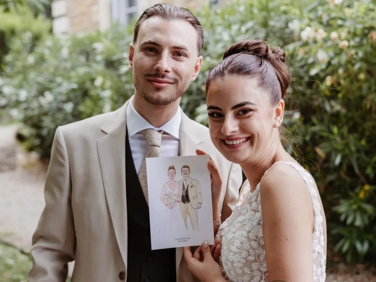 Un couple de mariés souriants posant à l'extérieur, tenant une carte illustrée de leur mariage.