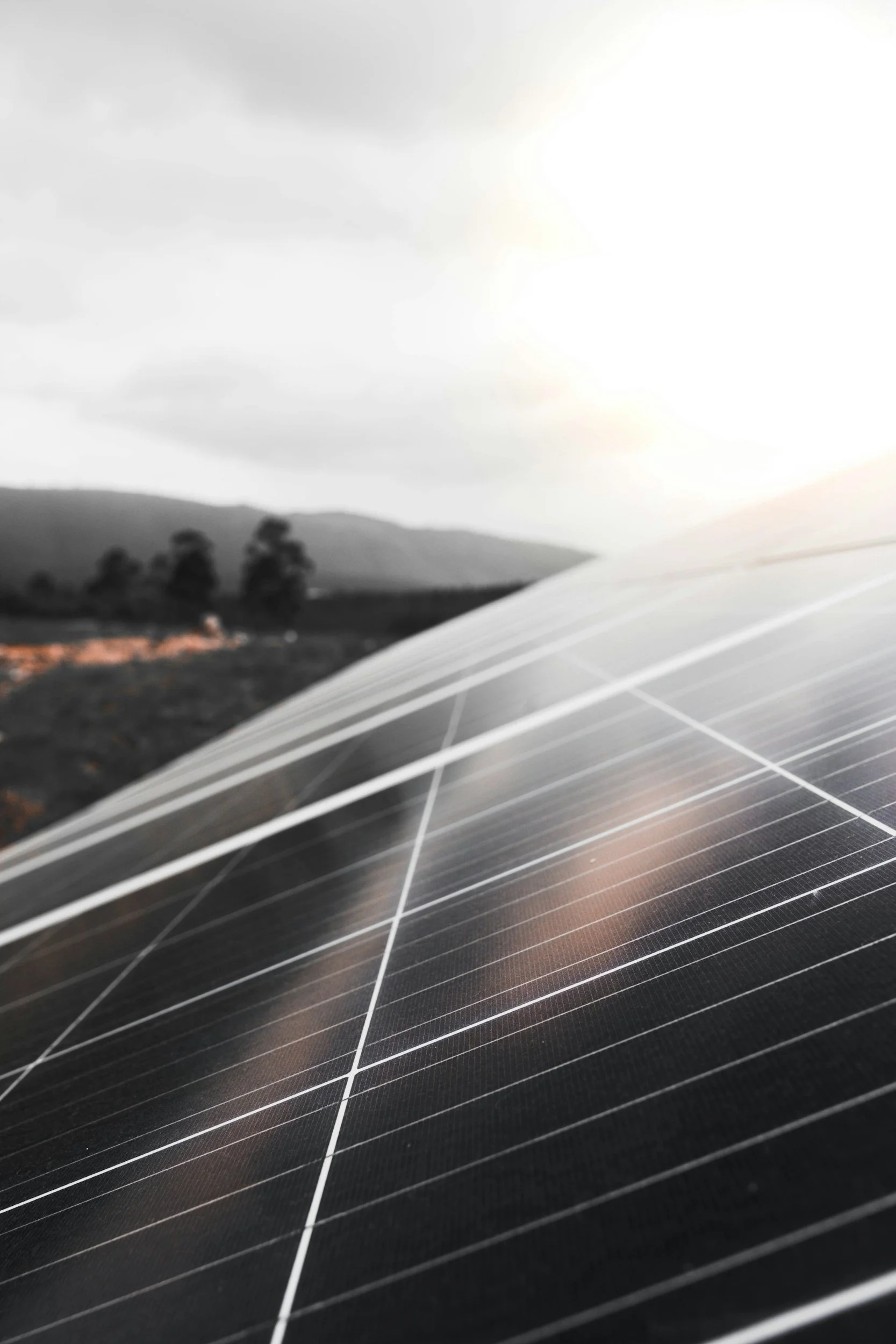 Close-up of solar panels with a blurred natural landscape and cloudy sky in the background.