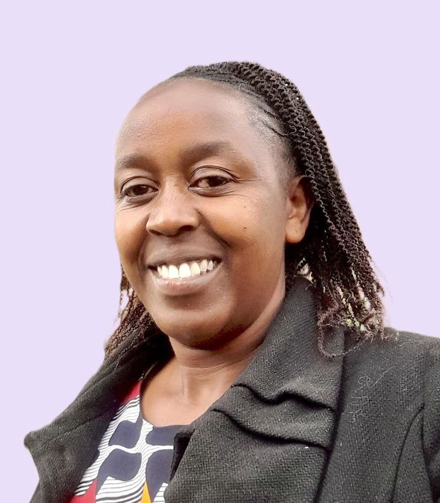 A woman smiling, wearing a black blazer and a patterned top, with braided hair against a light purple background.