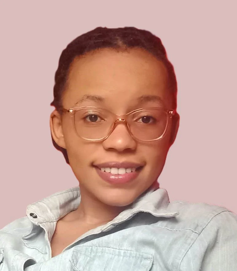 A young woman wearing glasses and a light-colored shirt taking a selfie against a pale pink background.