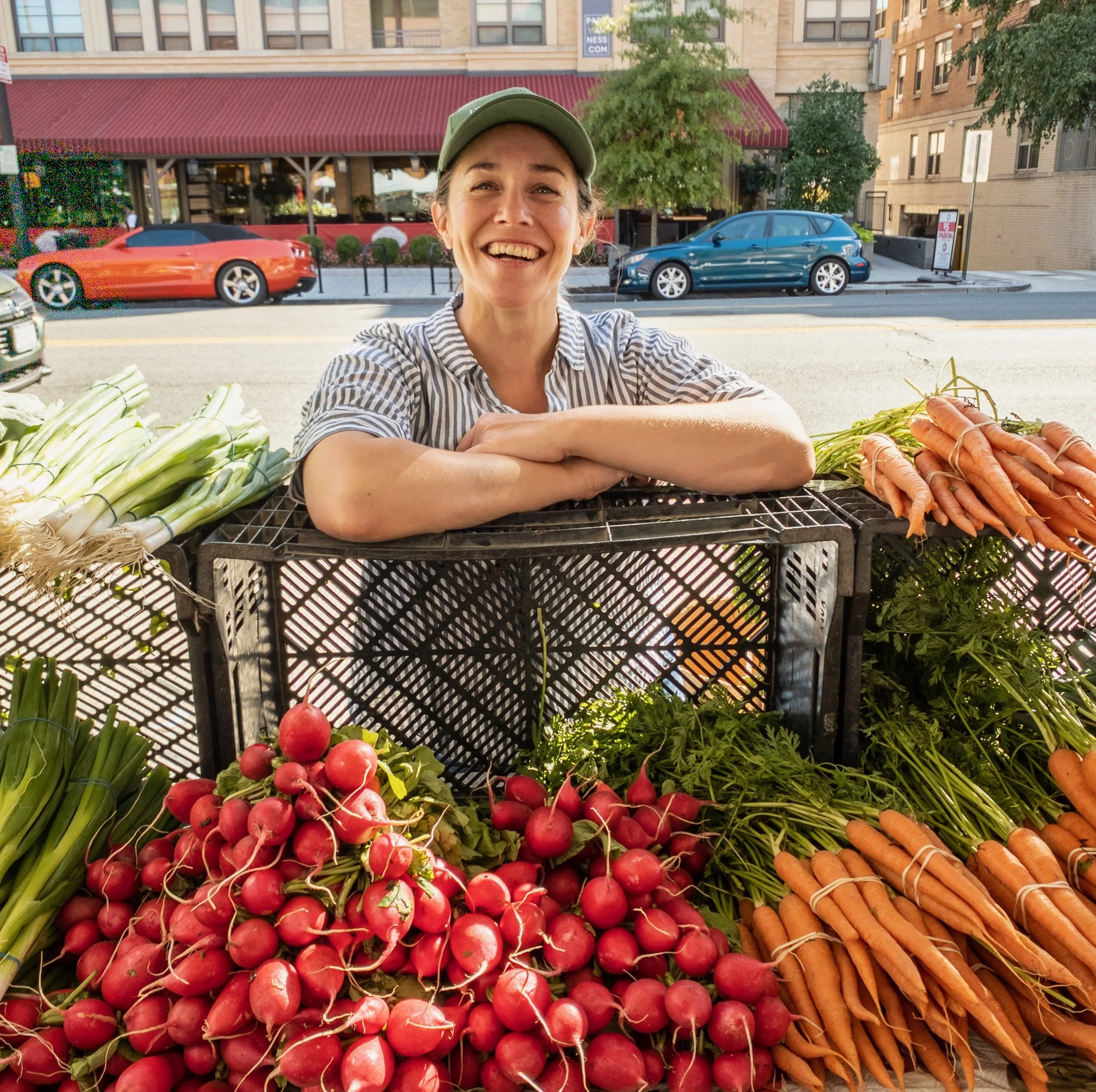 Woman smiling at a farmers market with fresh radishes and spring onions to donate to DC Food Rescue