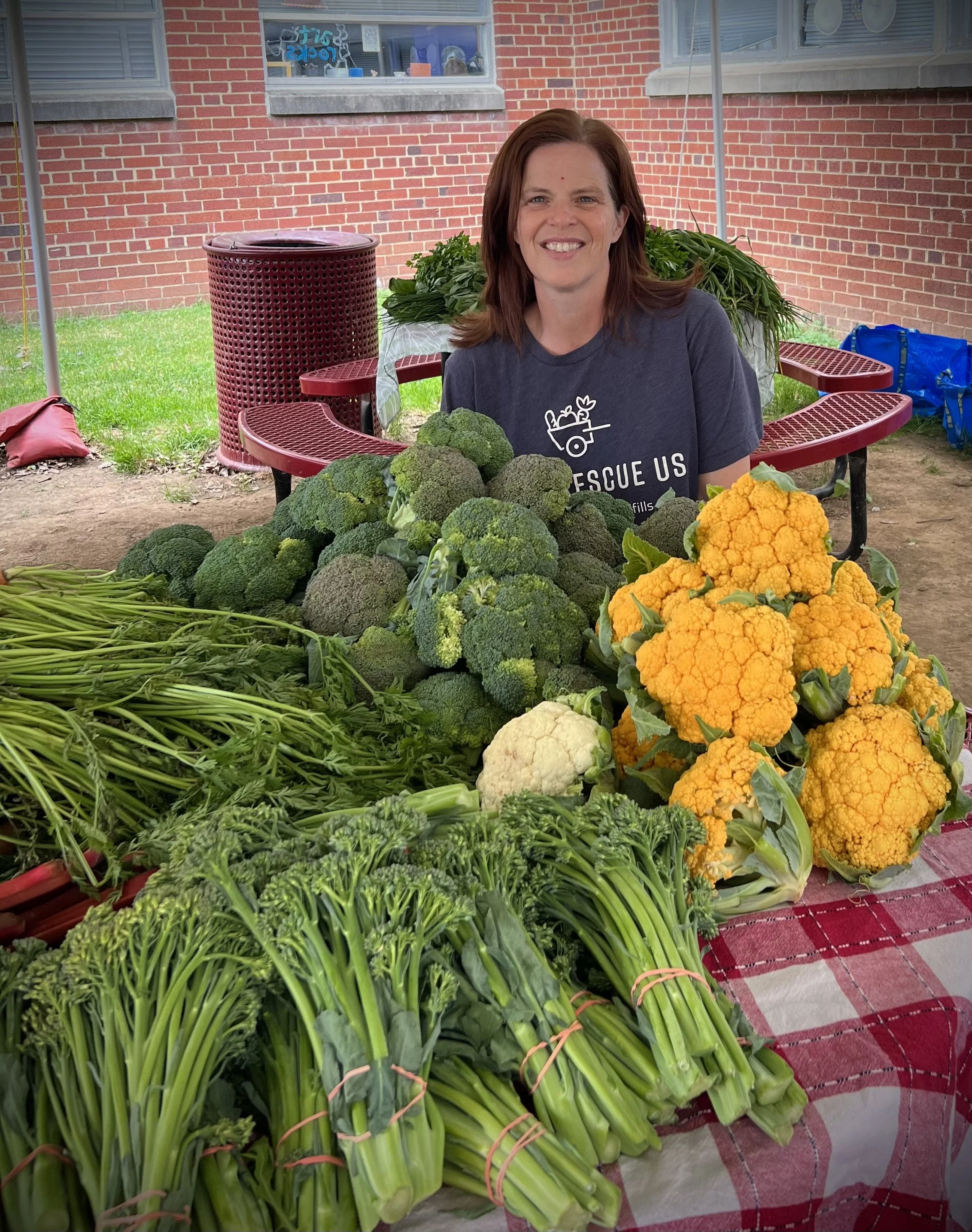 DC Food Rescue Operations Director Jenna Von Elling smiling with a large pile of broccoli and cauliflower donated from a farmers market.