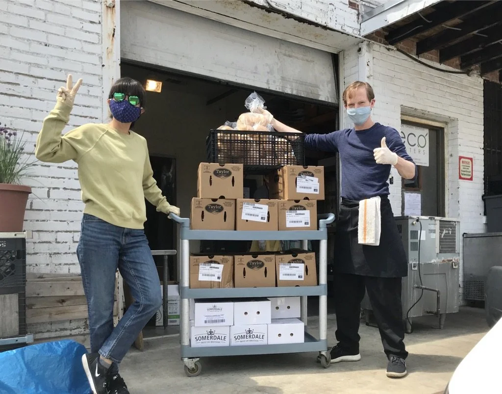 Two Eco Caters employees wearing COVID-19 masks giving a thumbs up next to a large donation of catered food to DC Food Rescue.