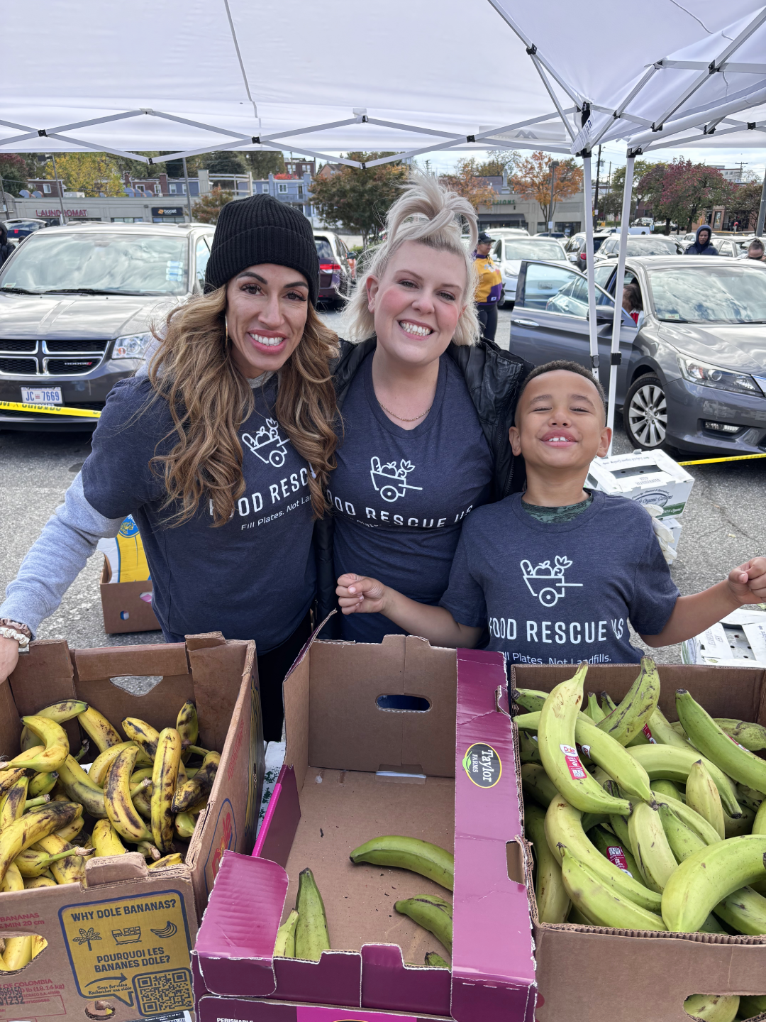 Three smiling volunteers at a Good Neighbors Market in October 2025