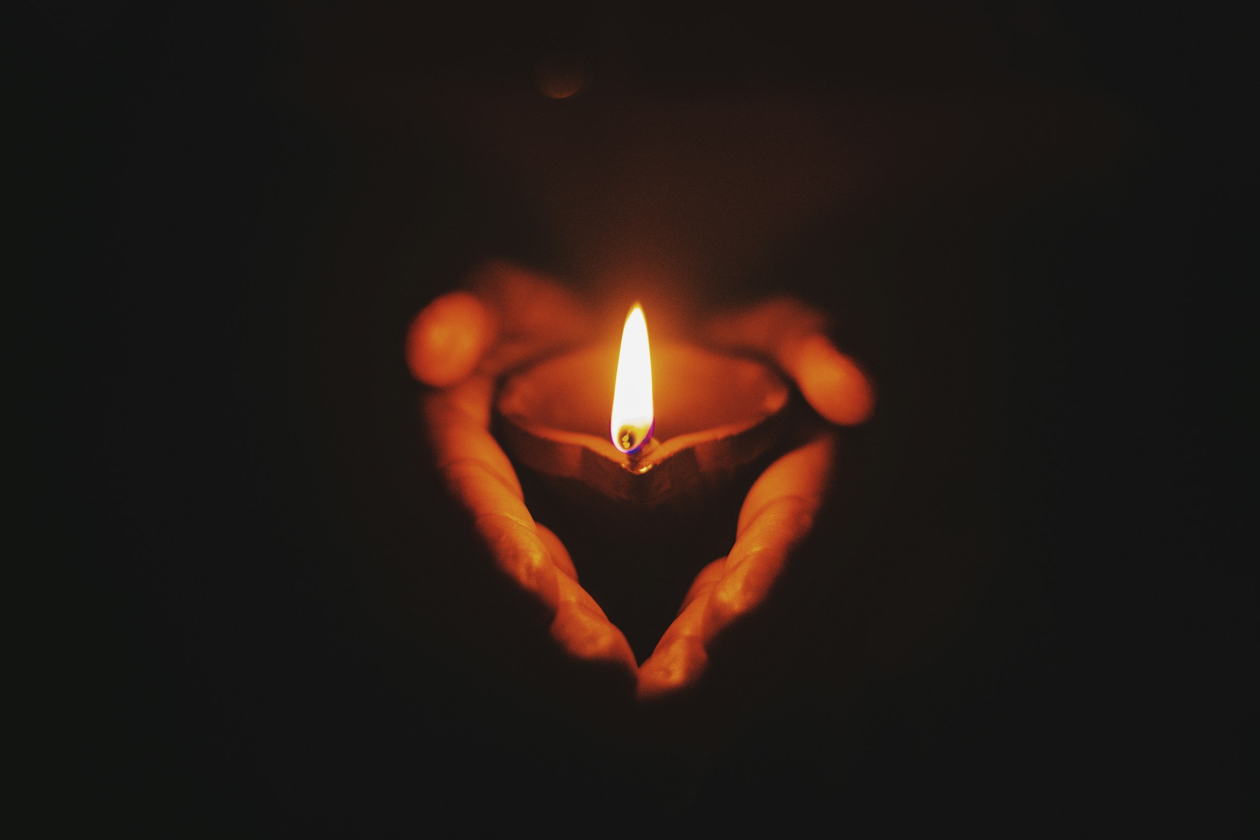 A hand holding a small tea light candle, lit, in a dark setting.