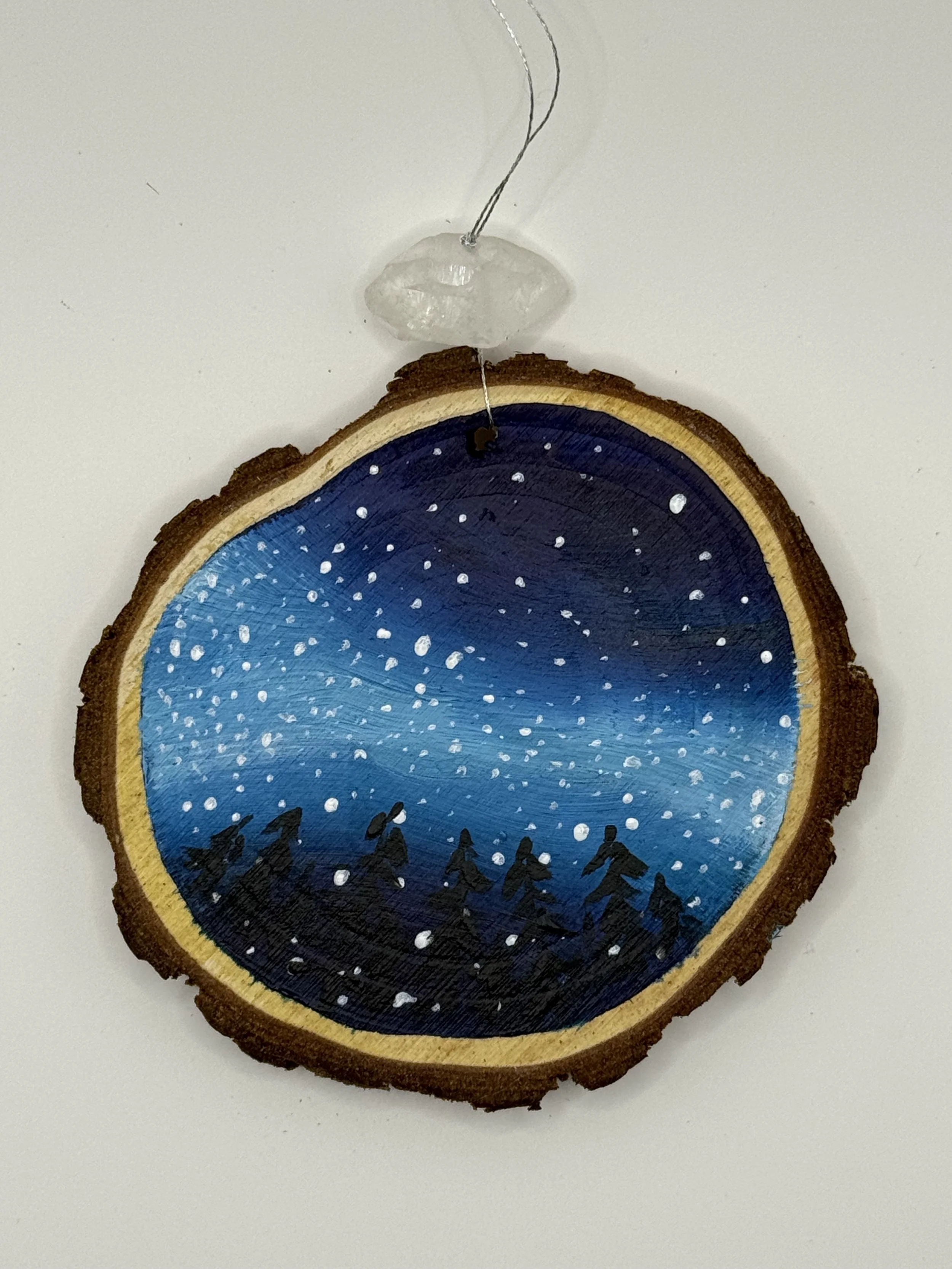 A cross-section of a wooden log painted with a night sky scene, including stars and silhouettes of trees, with a small crystal and wire above it for a paint-and-sip class hosted by CVU Acces.