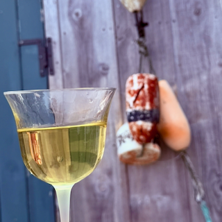 A glass of Chardonnay wine next to buoys hanging on the side of a wooden shed.