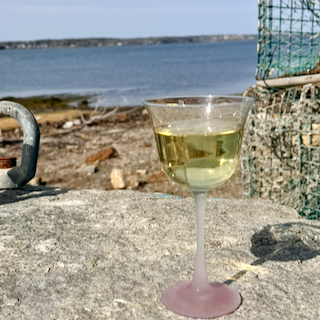 Glass of Chardonnay wine on a rock surface near the Maine coast with water and lobster traps in the background.