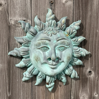 Decorative sun art wall hanging with a smiling face and sun rays, mounted on a wooden wall.
