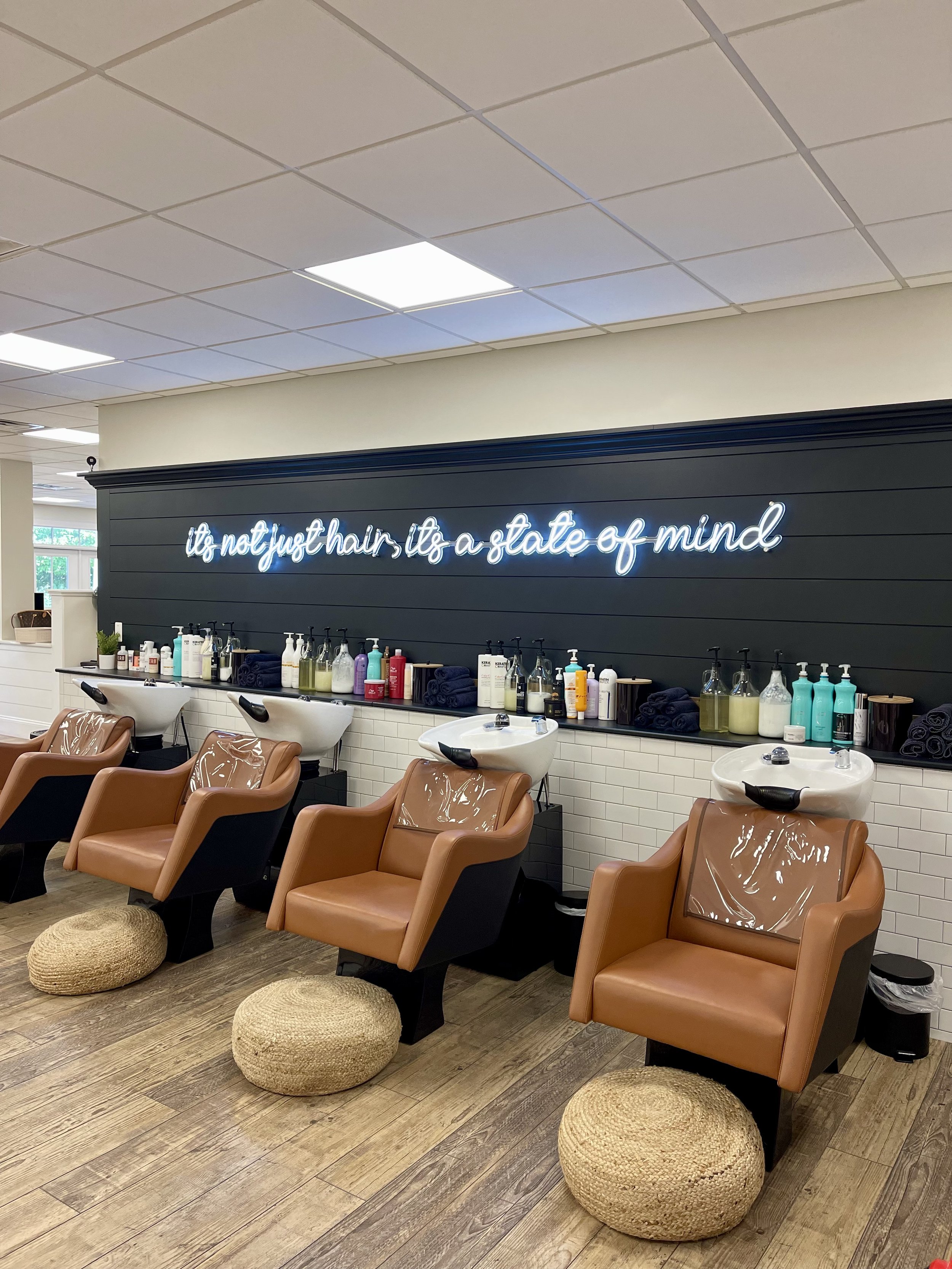 Salon chairs and washbasins in a hair salon, with a neon sign on the wall reading 'it's not just hair, it's a state of mind'.