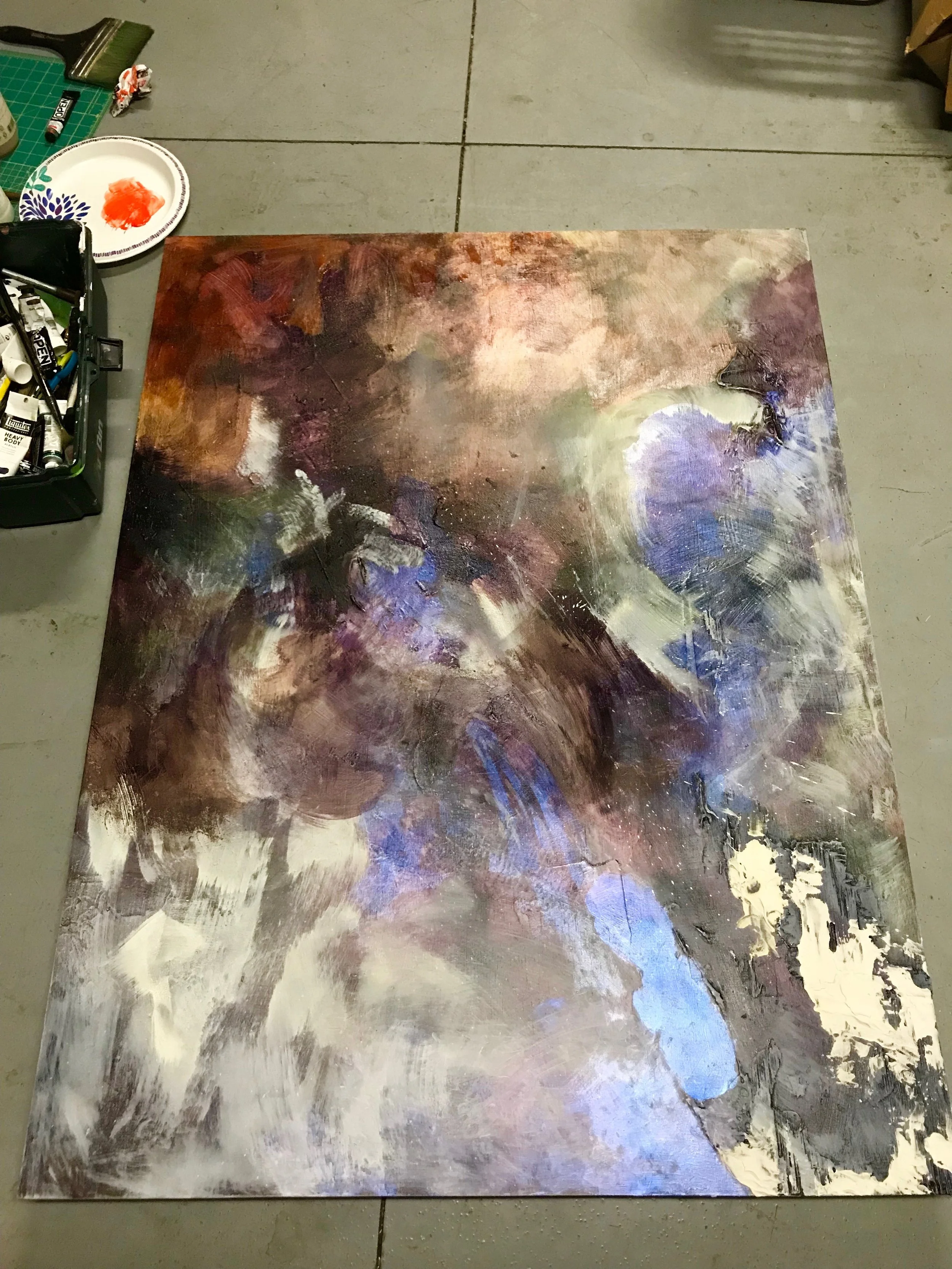 Rectangular painting panel on a garage floor with rough dashes of brown, white, black, gray, and iridescent blue.
