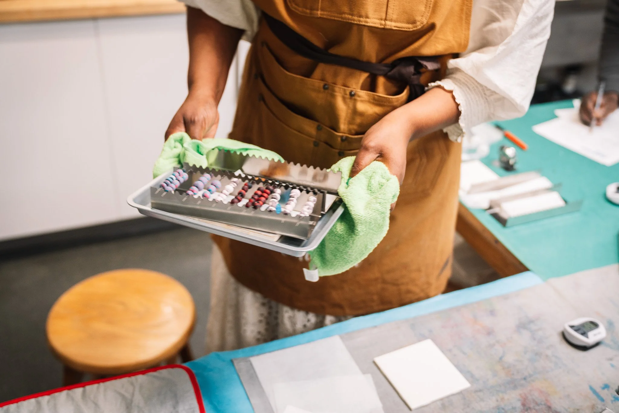 A person wearing a brown apron and holding a tray of various colored pills or tablets in a healthcare or pharmacy setting.