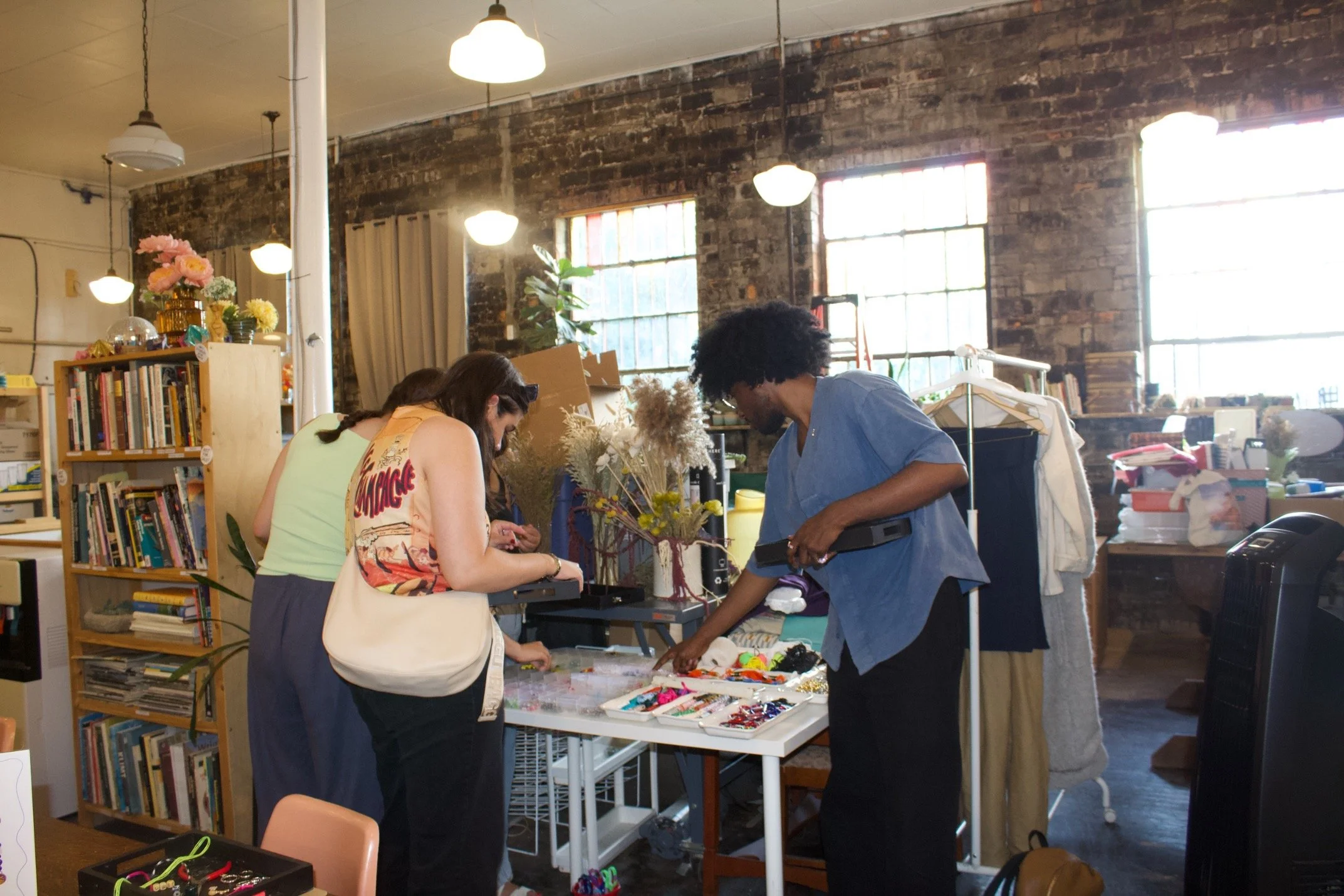 People browsing through items at a flea market or thrift store in a rustic, industrial-style space with brick walls and large windows.