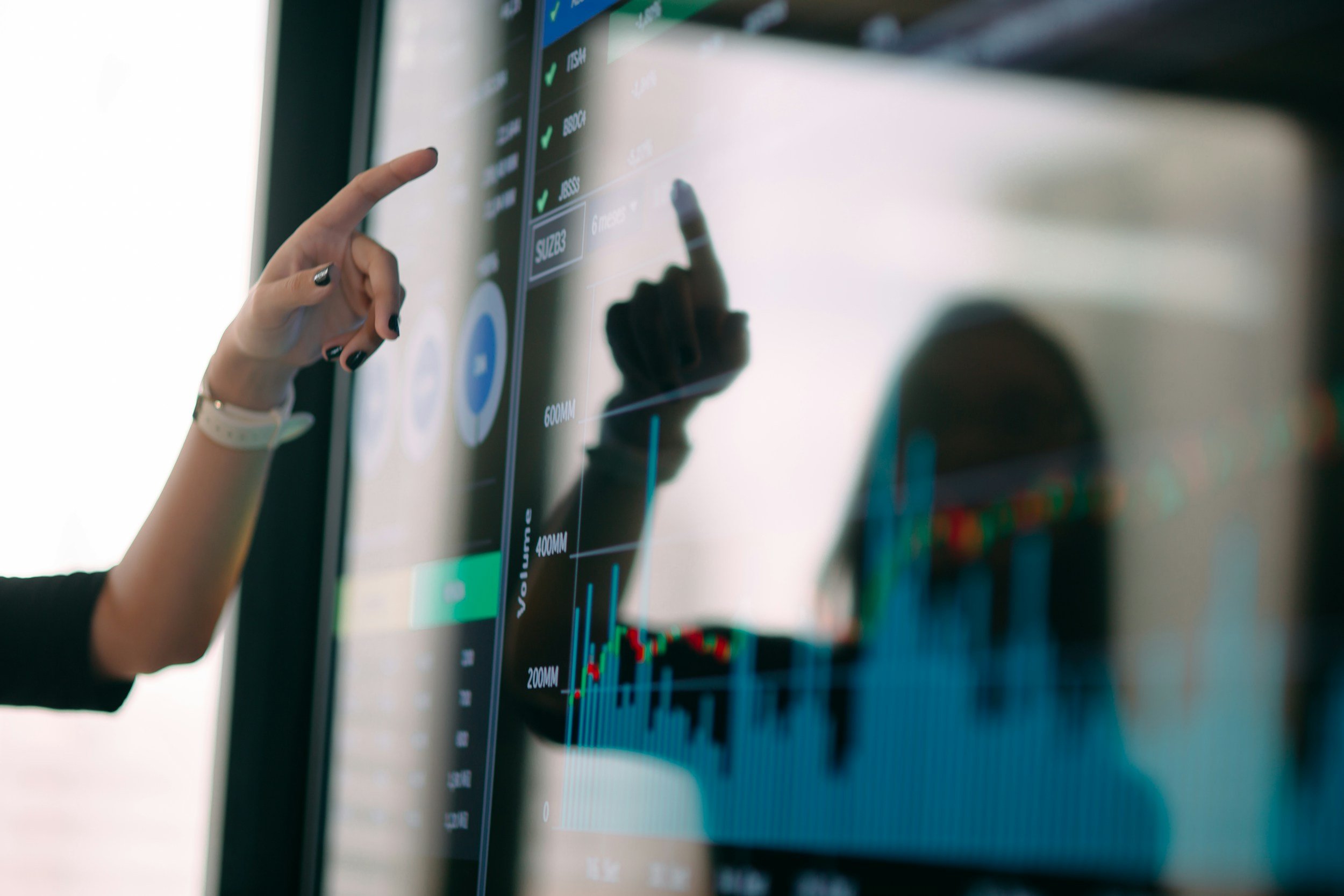 Close-up of a person's hand pointing at a digital screen displaying graphs and data.