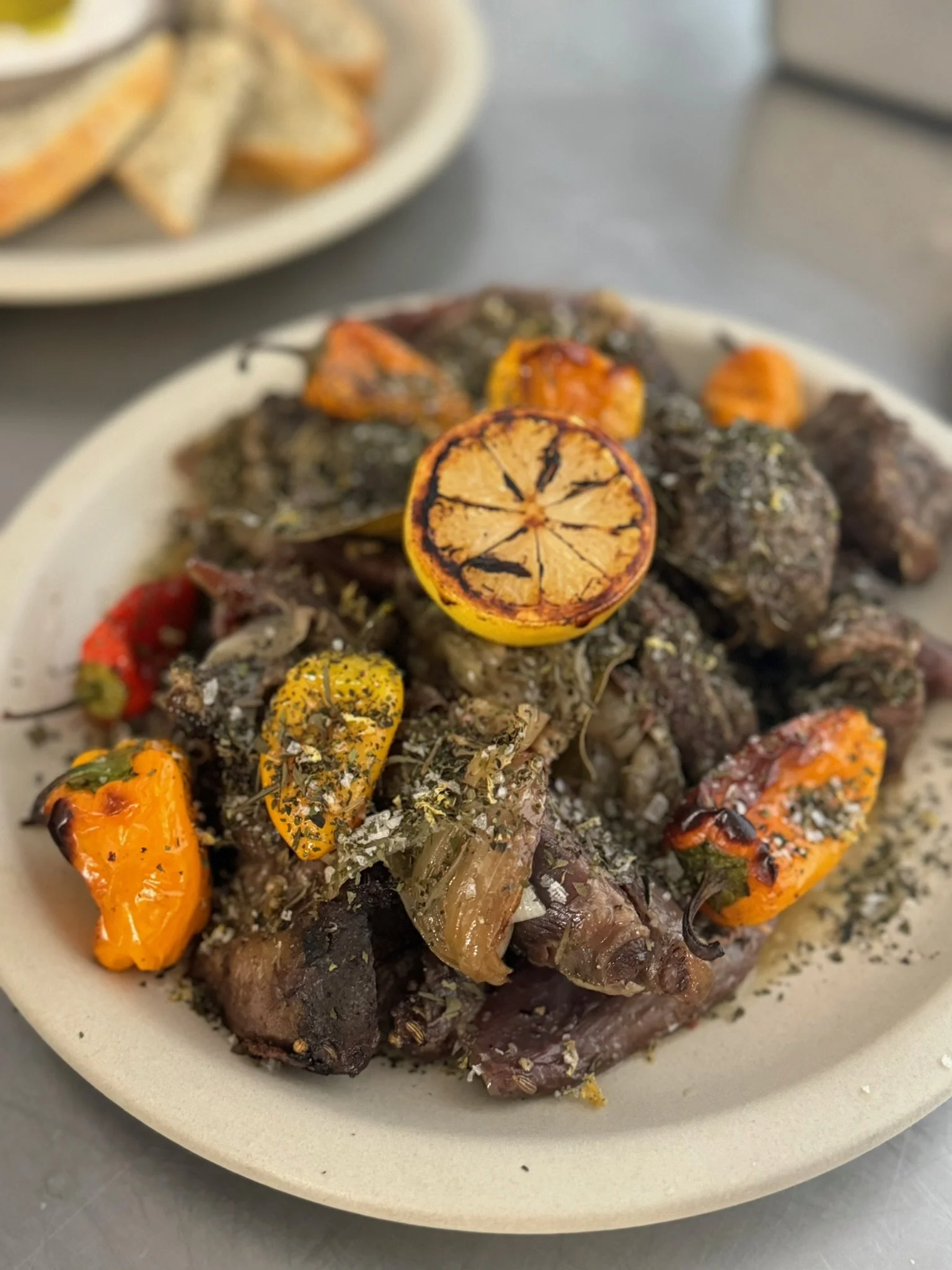 A plate of cooked beef liver garnished with grilled lemon slices, roasted peppers, and herbs.