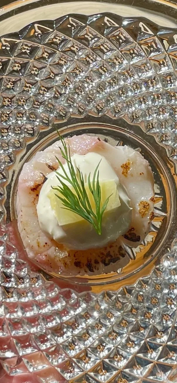 Close-up of a dish with a dollop of sour cream, a small pat of butter, a sprig of dill, and some fish fillet on a decorative glass plate.