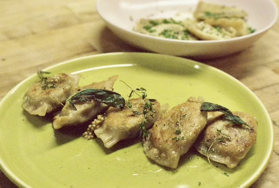 Four pan-fried pierogi garnished with sage on a green plate.