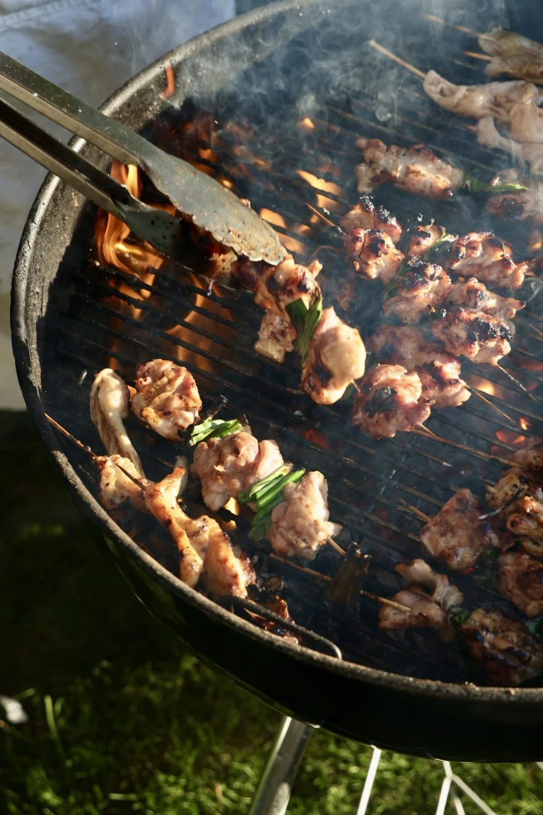 Skewers with grilled meat cooking on a barbecue grill over open flames, garden party in Chilmark.