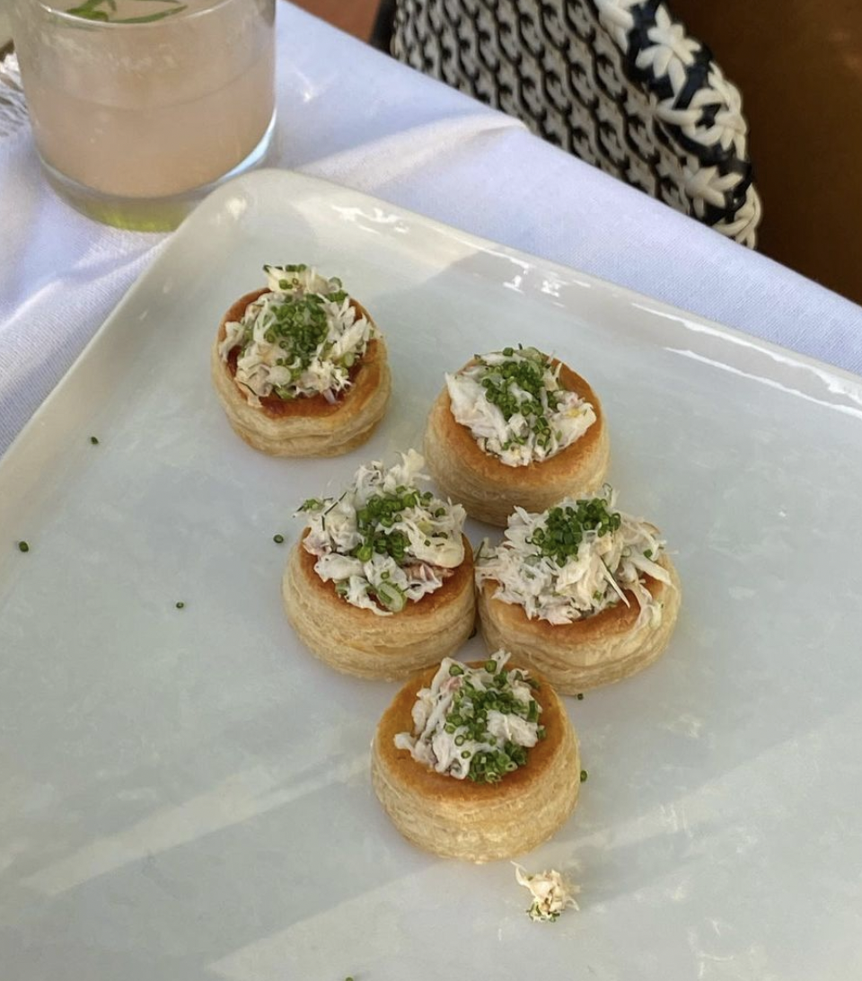 Five mini crab cakes topped with chopped green onions, served on a white rectangular plate.