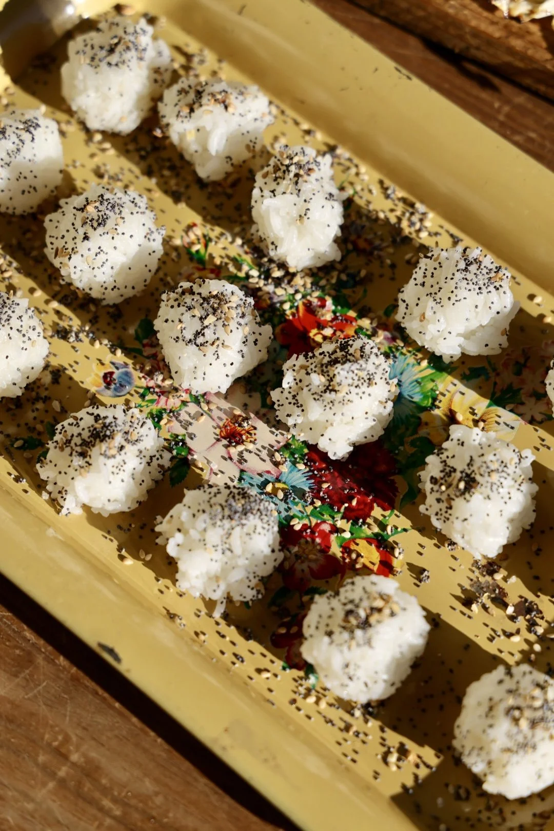 Small white rice balls topped with black sesame seeds, on a colorful floral tray, at a garden party in Chilmark.