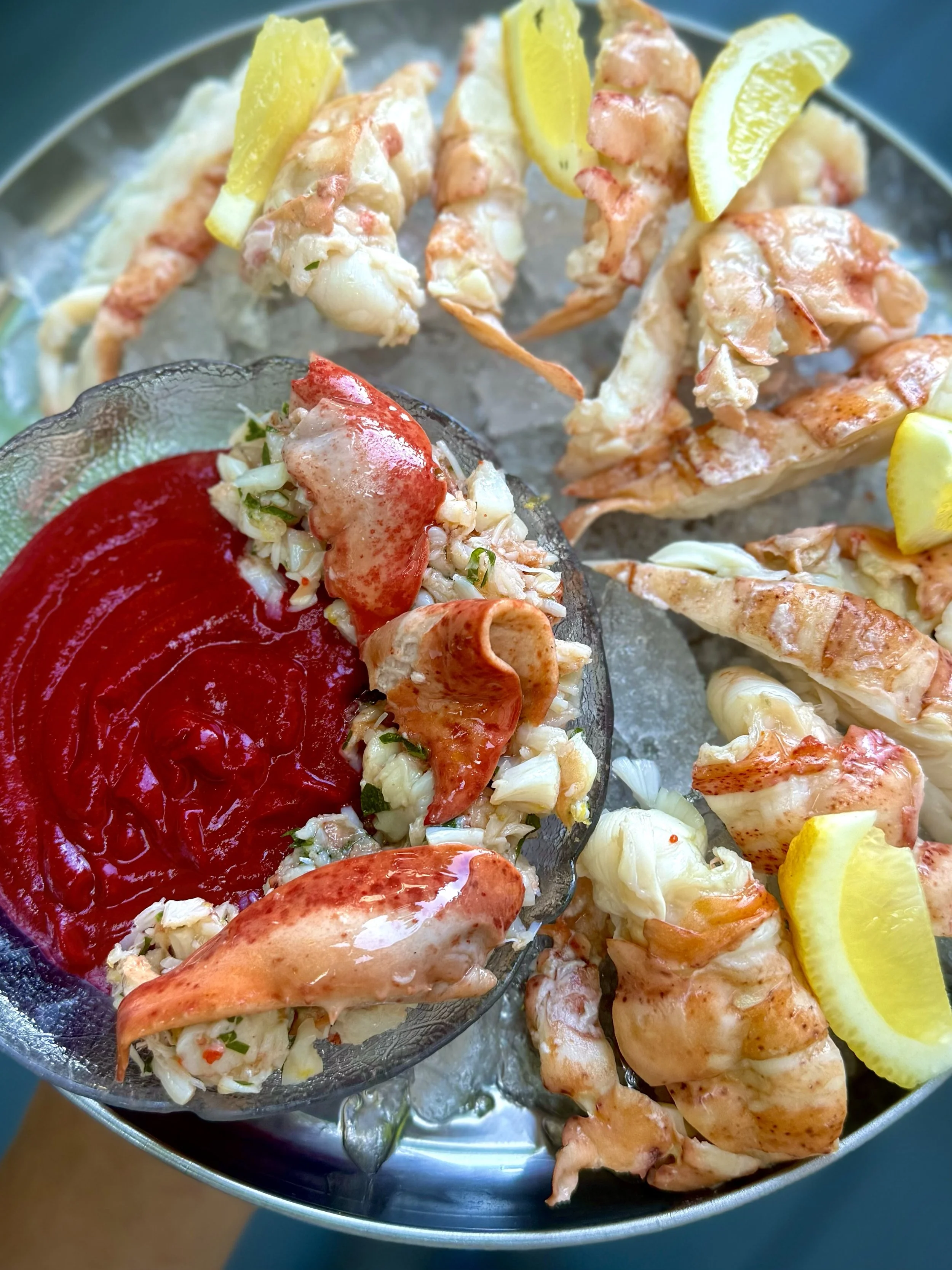 Lobster claws and tails with lemon wedges served with cocktail sauce and a seafood salad.