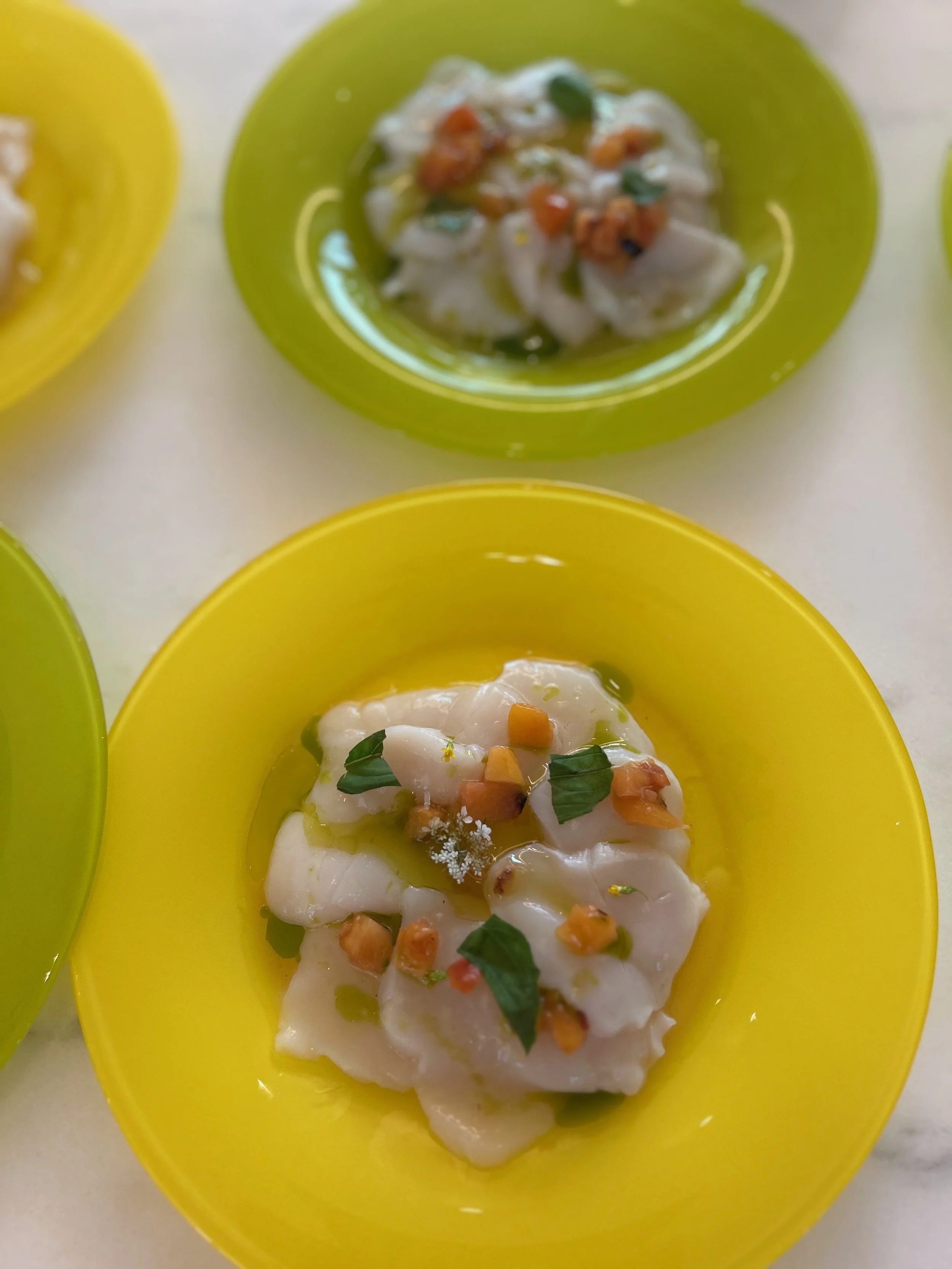 Close-up of two yellow bowls containing raw fish fillets garnished with herbs, spices, and oil.