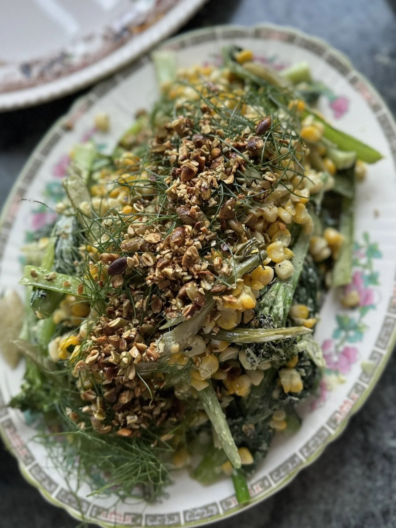 Fresh chopped vegetables topped with crushed nuts and herbs on a decorative oval plate.