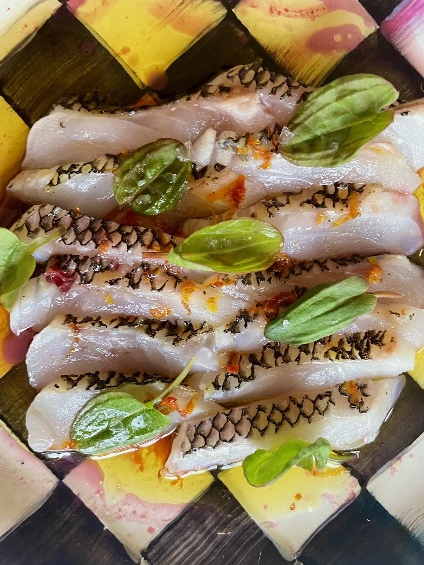 Fresh fish fillets garnished with green herbs and spices, arranged on a colorful plate.