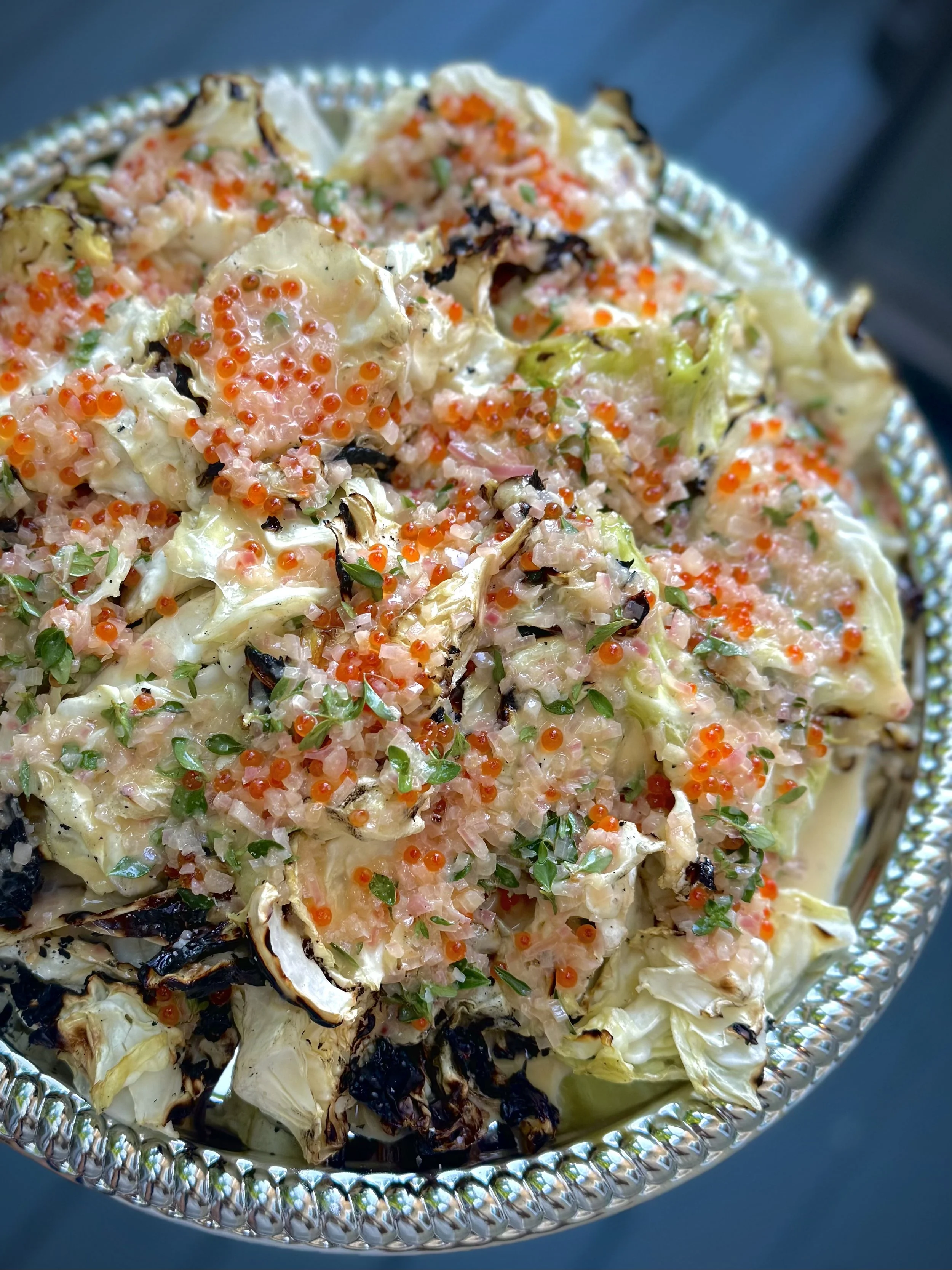 Roasted cauliflower topped with chopped onion, cilantro, and orange fish roe, served in a decorative silver bowl.