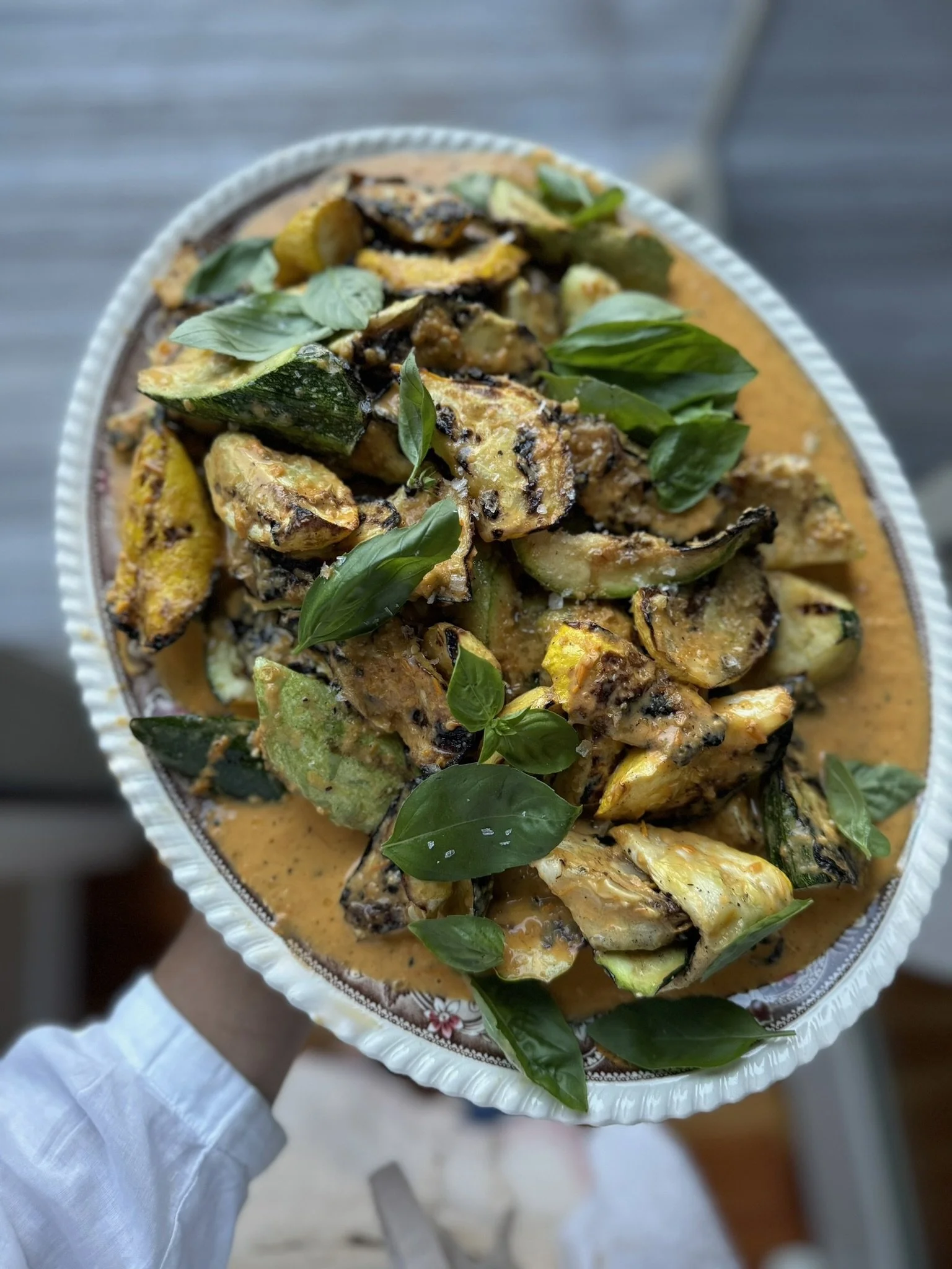 A dish of roasted zucchini topped with fresh basil leaves in an orange creamy sauce.