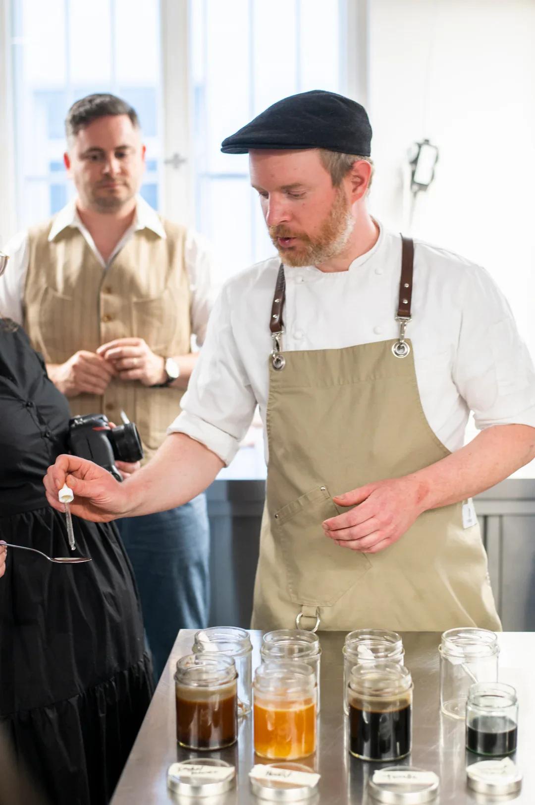 Ein Koch erklärt mehreren Personen die Unterschiede zwischen verschiedenen Kaffeeproben in Gläsern.