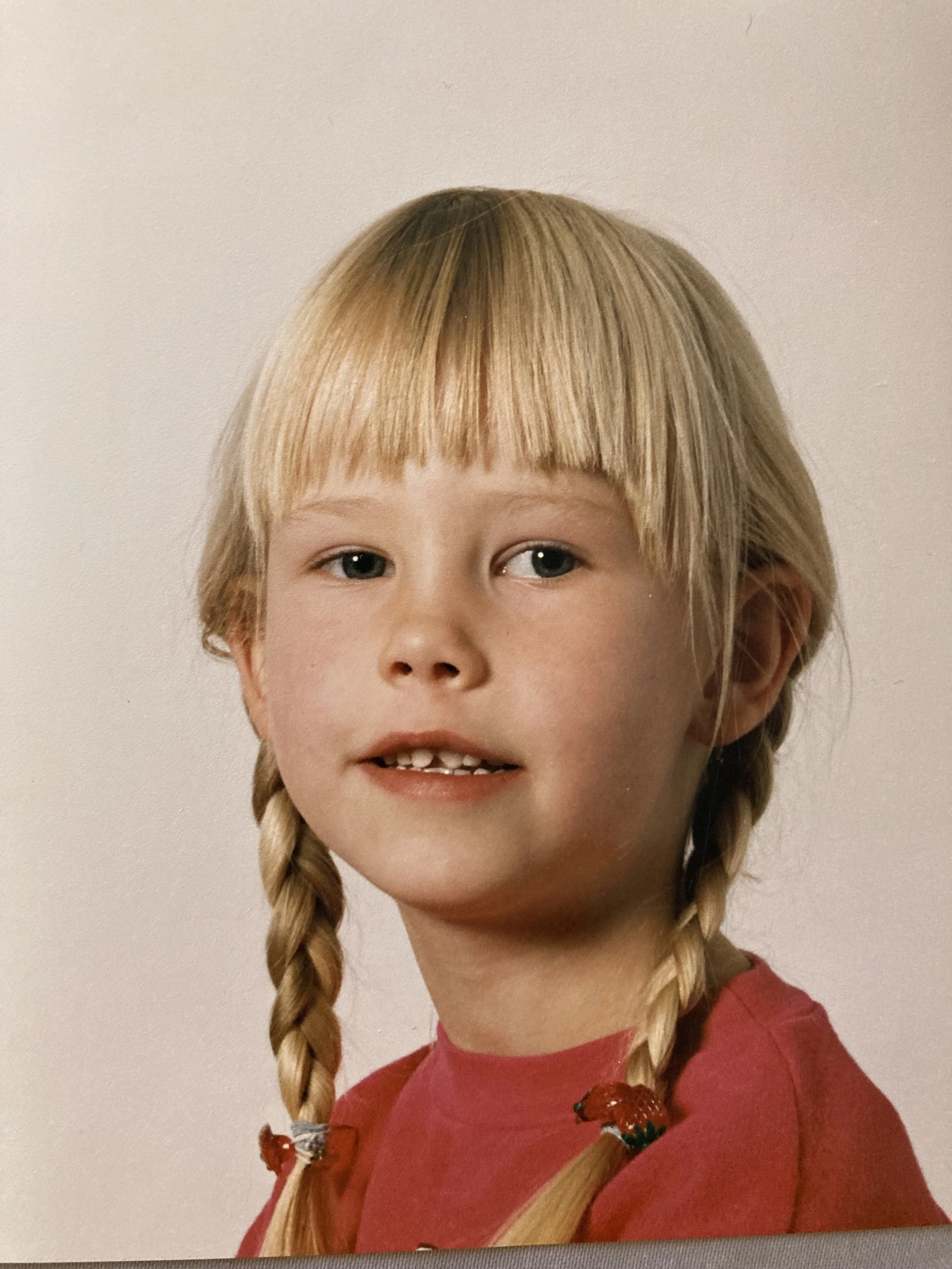 Ein junges Mädchen mit blonden Haaren in Zöpfen trägt ein rotes Oberteil.