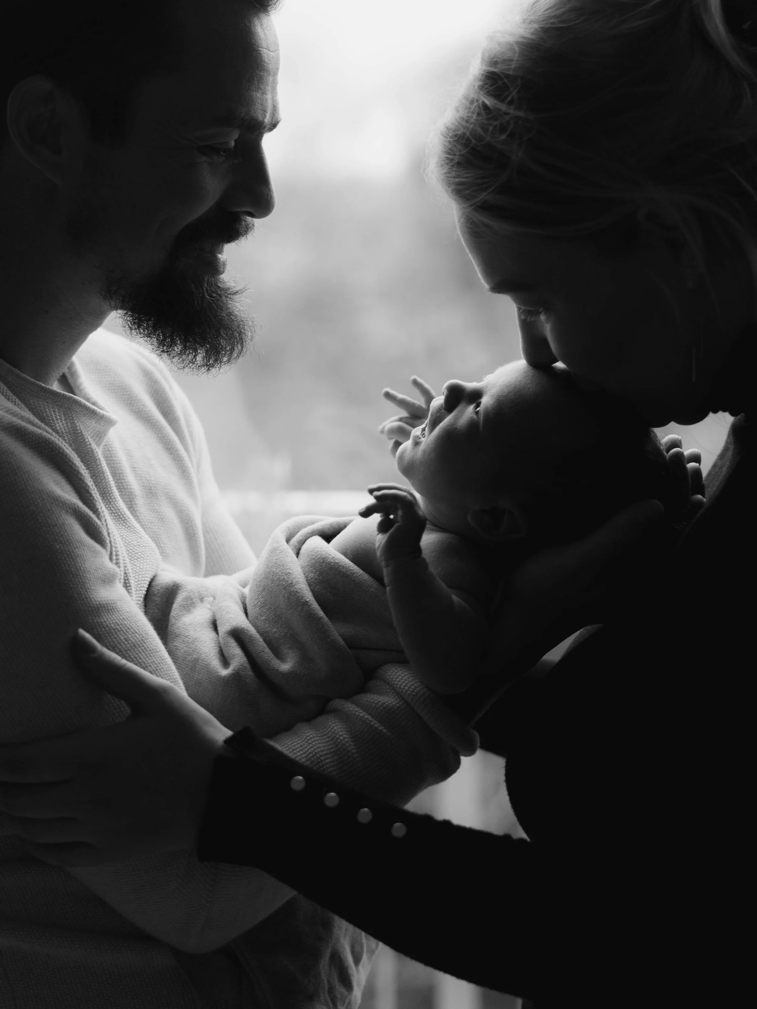 Zwart-wit foto van een man en vrouw die hun baby vasthouden en kussen.