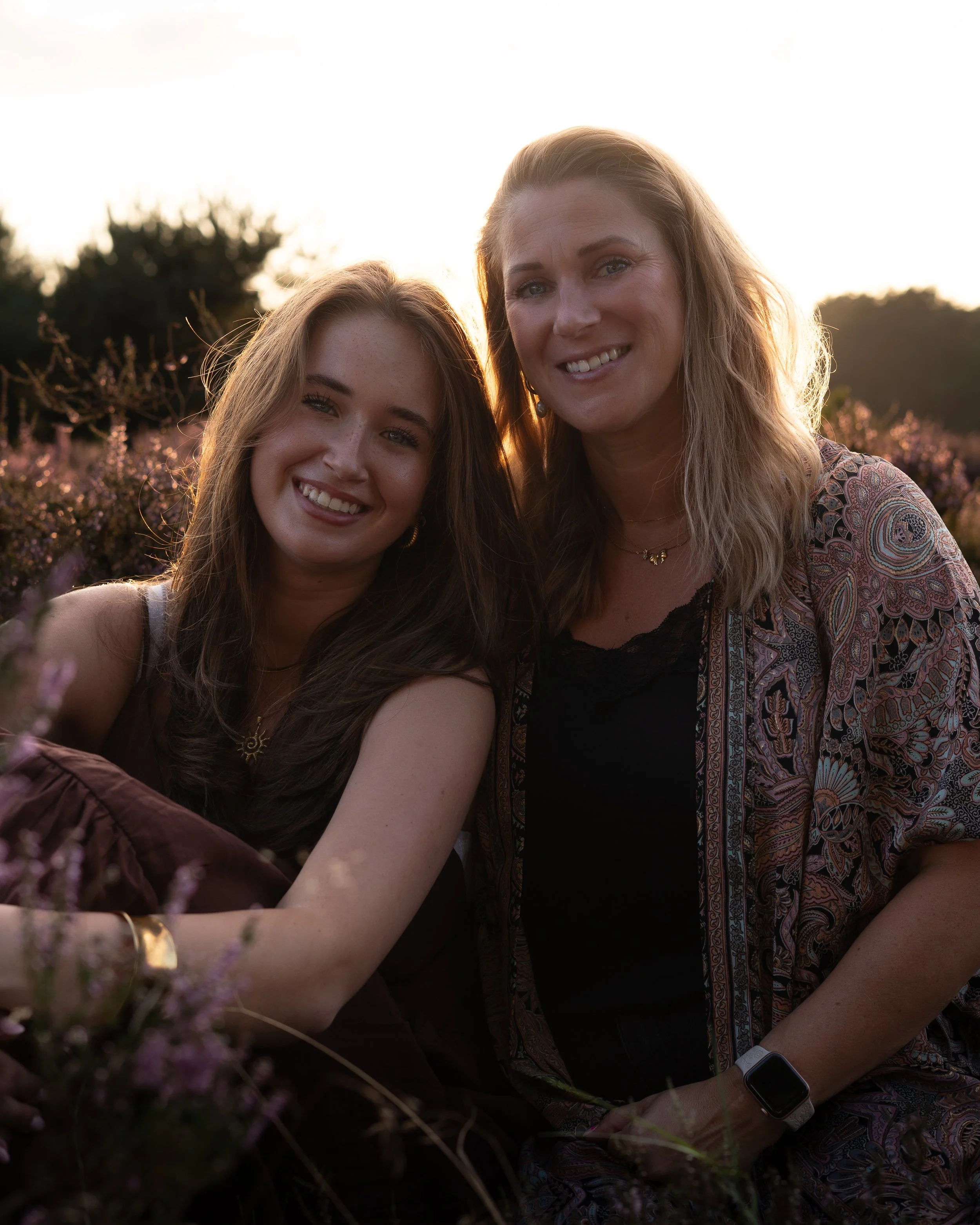 Twee vrouwen glimlachen in een bloemenveld bij zonsondergang.