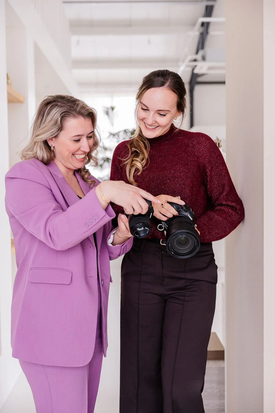 Twee vrouwen kijken samen naar een camera in een moderne, lichte interieurruimte.