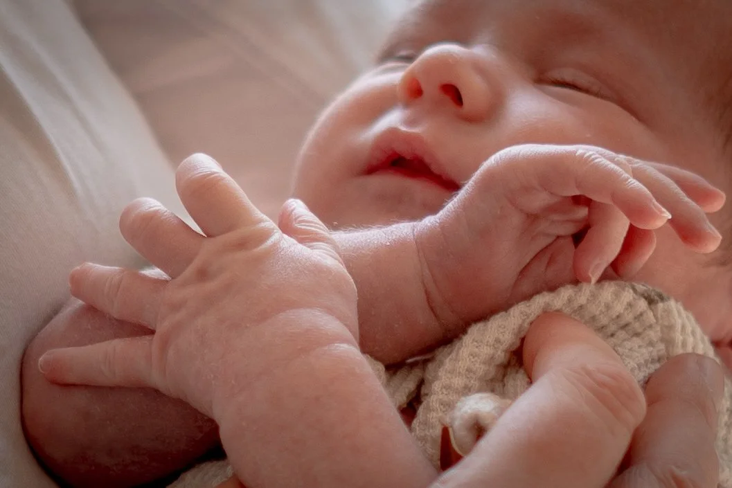 Een slapende baby met een moeder die haar hand op de schouder van de baby rust.