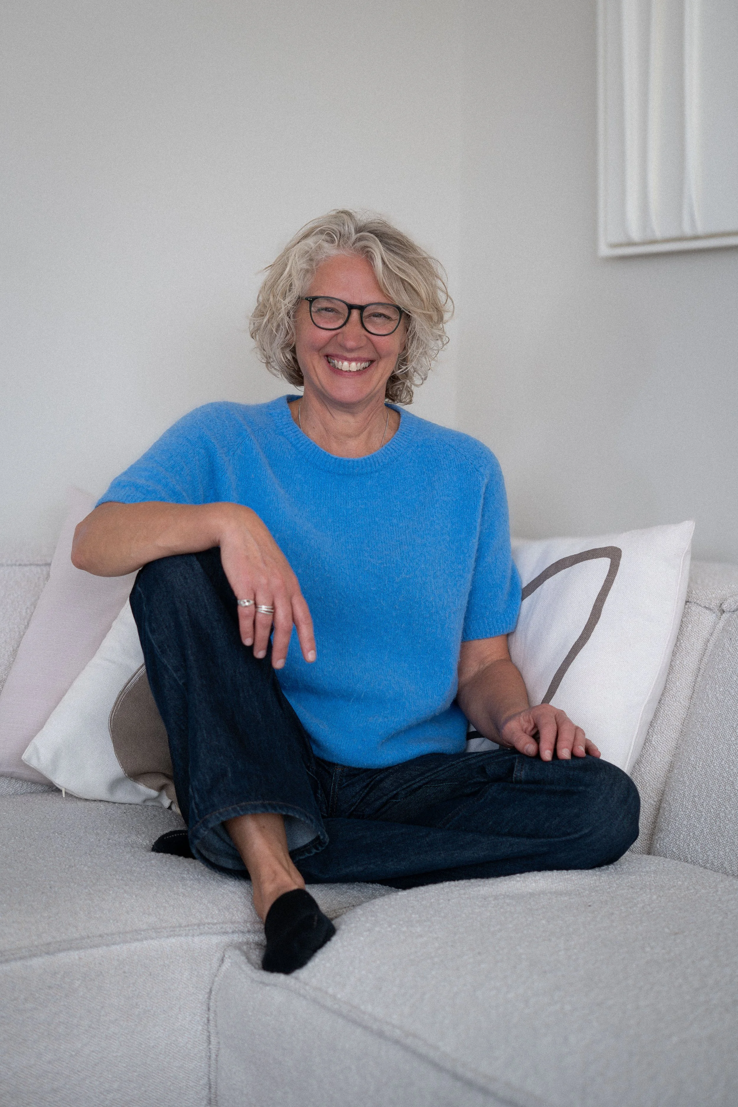 Vrouw houdt een smartphone met een foto galerij omhoog, omgeven door groene bladeren, lachend en in een binnenruimte.