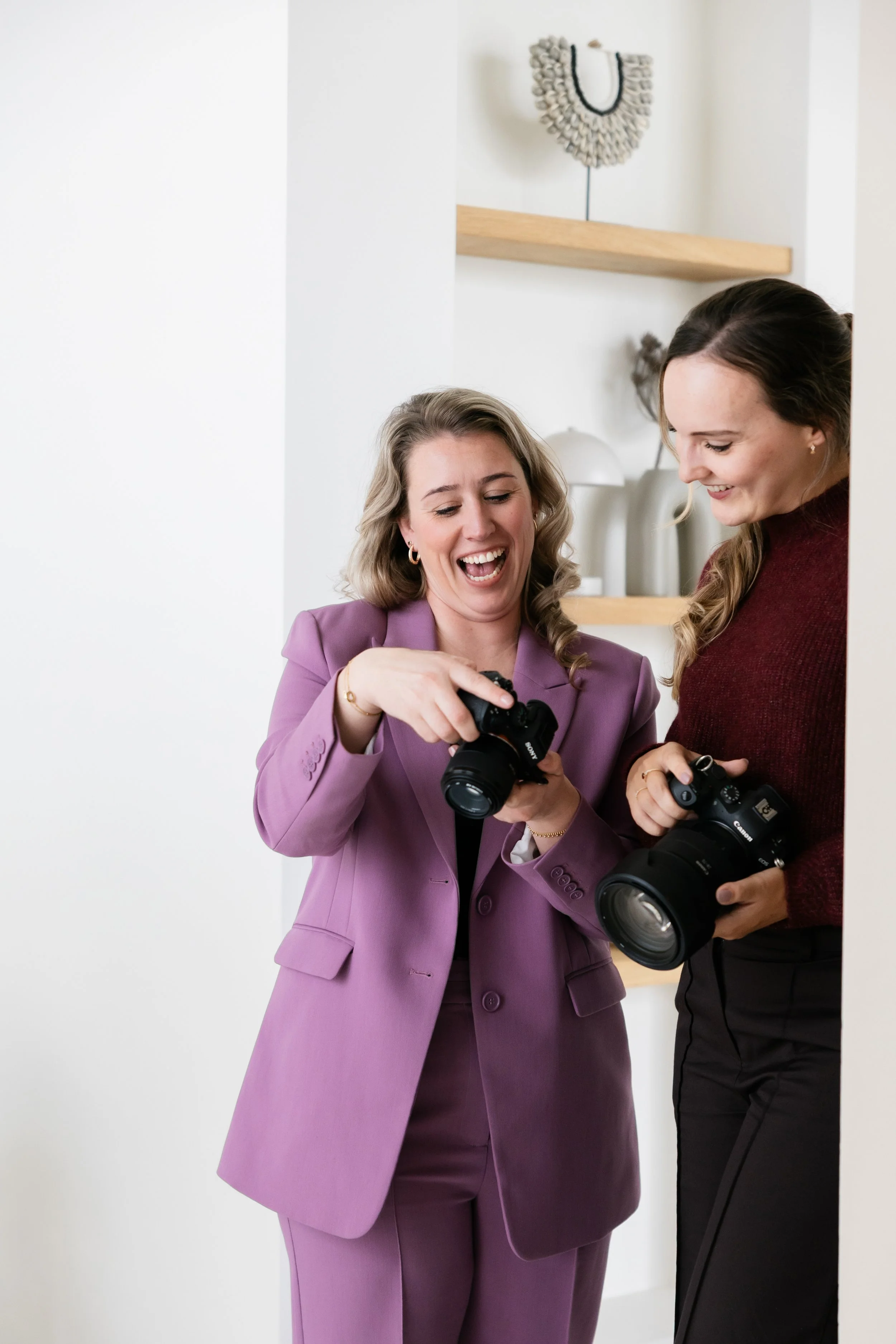 Twee vrouwen lachen en bespreken foto's met camera's in een lichte, moderne interieurruimte.